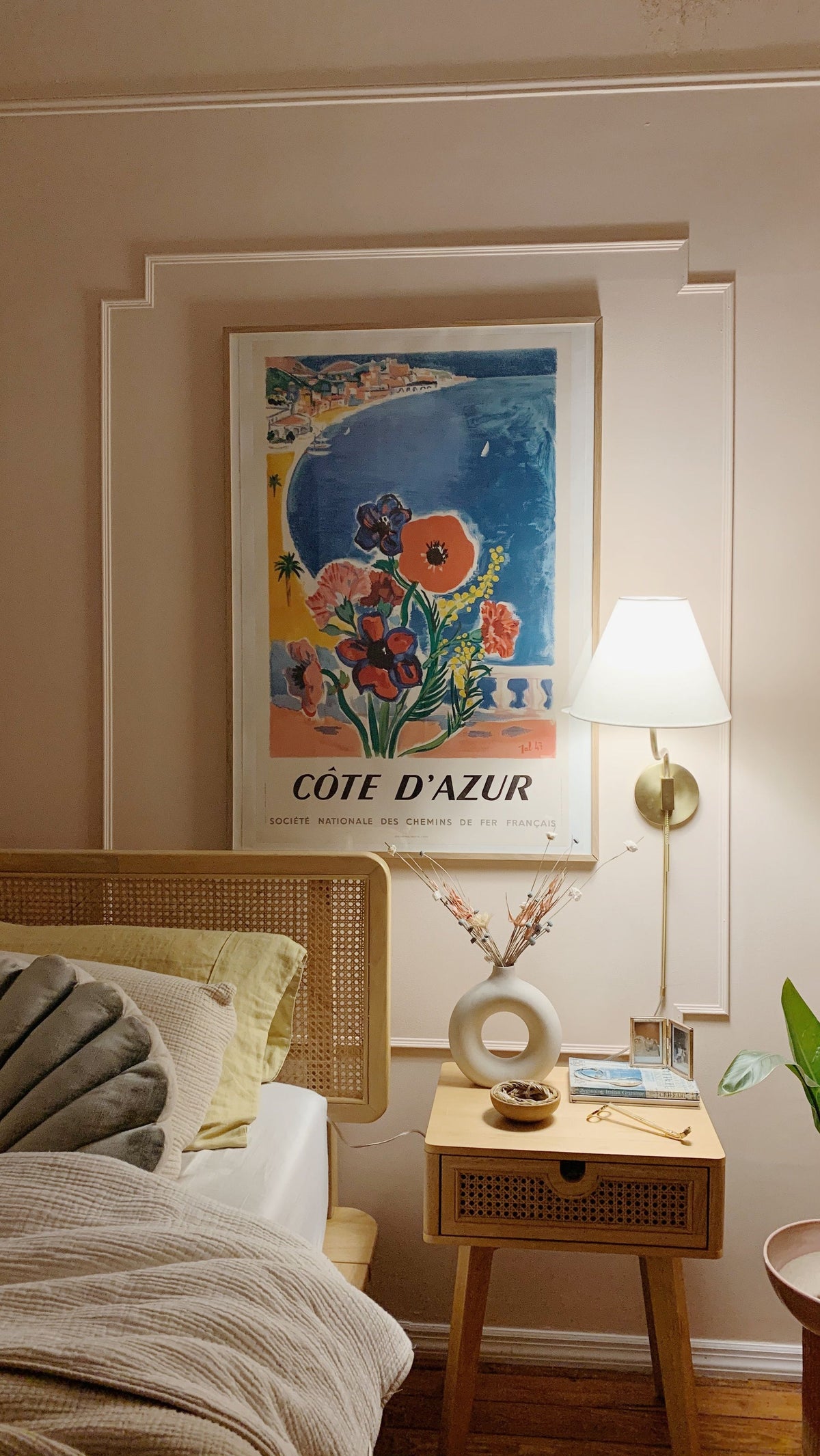 Patti brass plug-in wall sconce with a white linen shade mounted next to a bed