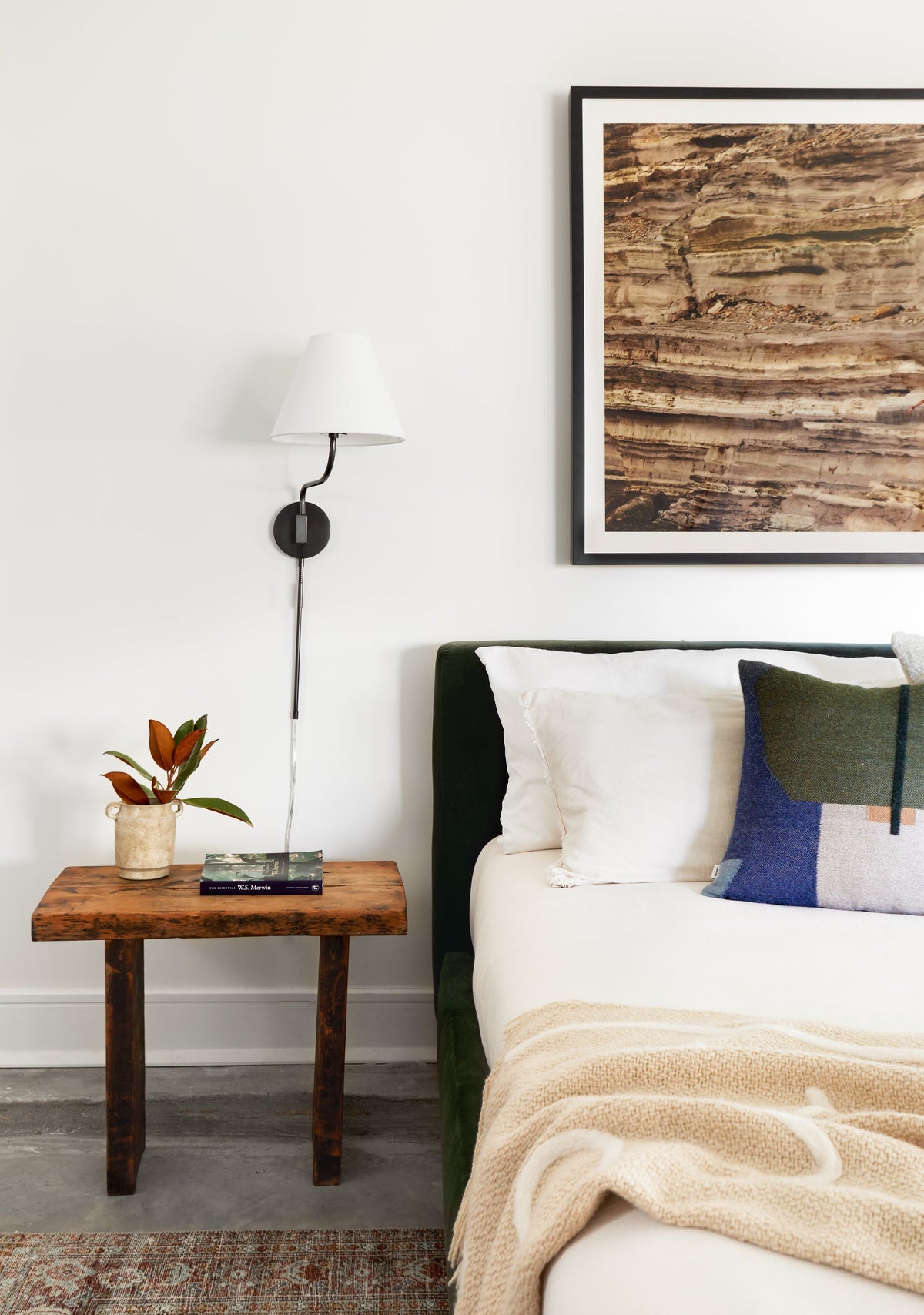 Patti plug-in sconce with white linen shade and dark metal arm mounted above a wooden bedside table.