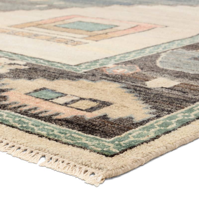 Reza hand-knotted wool rug corner with muted blue, cream, and pink geometric patterns and fringe.