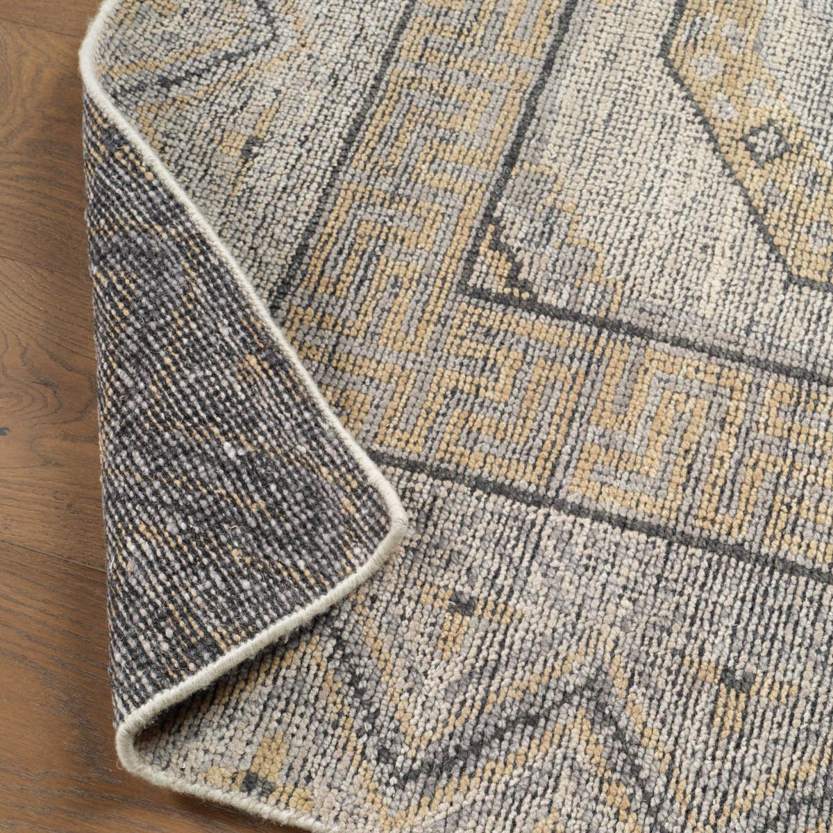 Rhapsody brown hand-knotted wool rug with a muted geometric pattern and folded corner showing the backing.