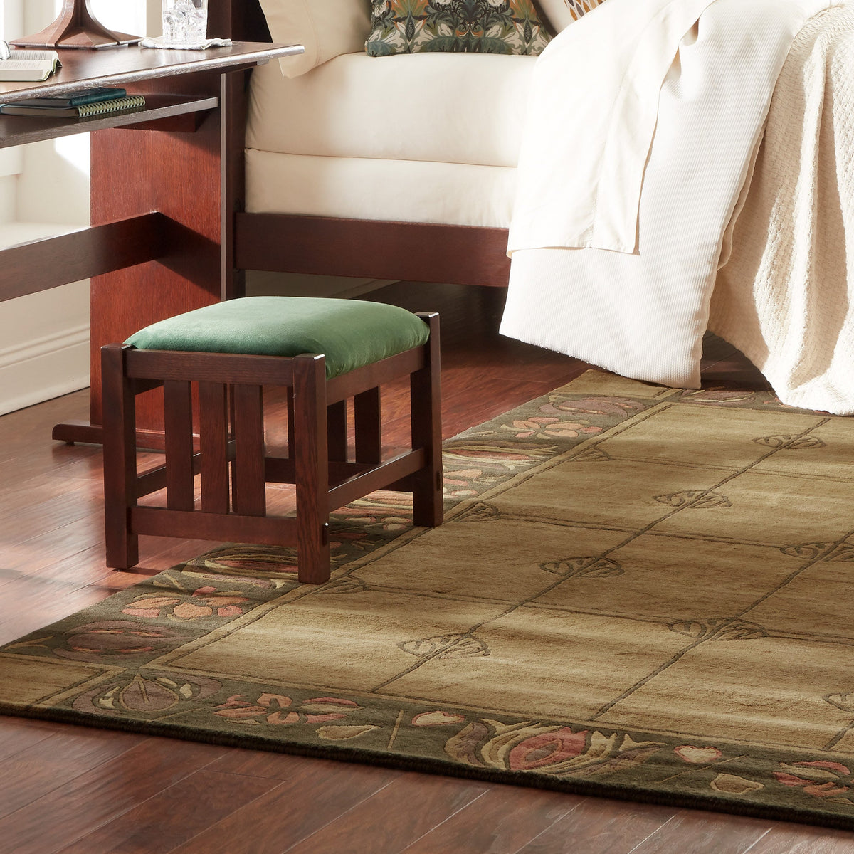 Mackintosh Stickley Windyhill olive green wool rug with floral borders next to a wooden footstool.