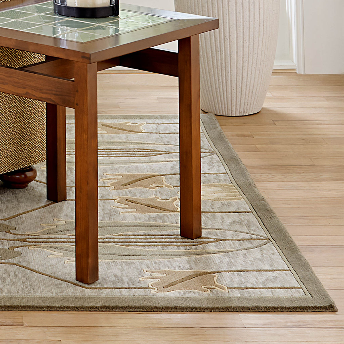 Rennie Tulip Stickley sage wool rug with geometric tulip motifs under a wooden table.
