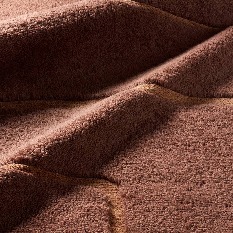 Solum hand-woven wool rug in terracotta with a thick, textured pile and carved wavy lines.