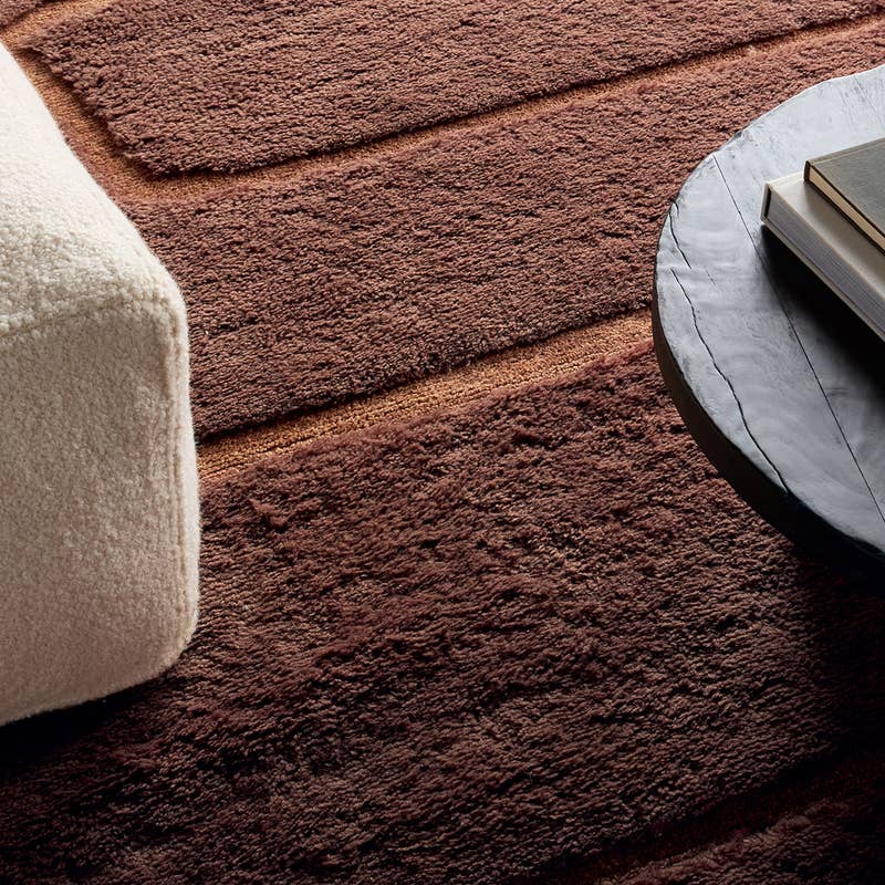 Solum hand-woven wool rug in brown with a thick, textured pile next to a white boucle ottoman.