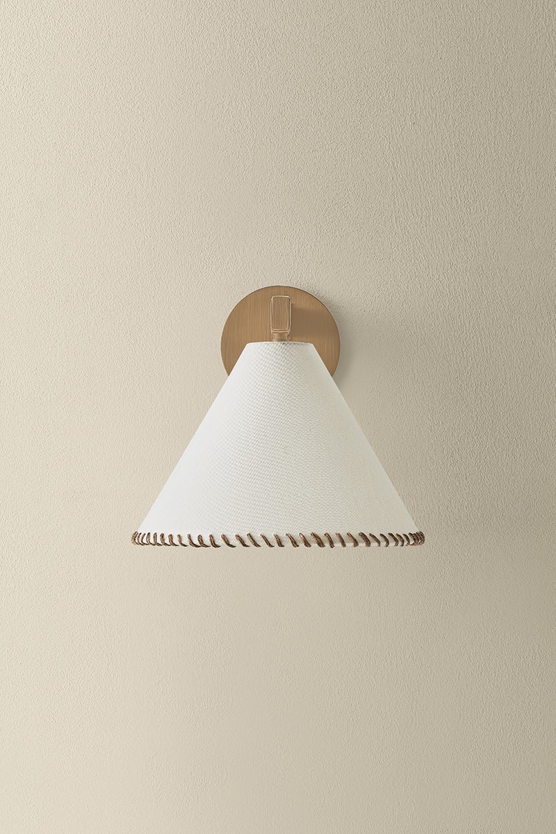 Stonely wall sconce with a white linen conical shade, whip-stitch trim, and patina brass mount.