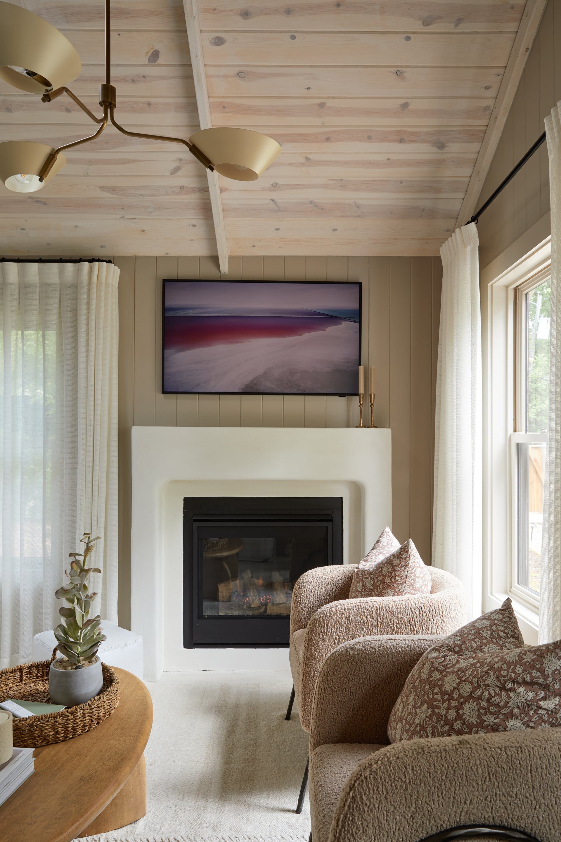 Sacramento brass chandelier hanging in a cozy living room with a fireplace and armchairs.