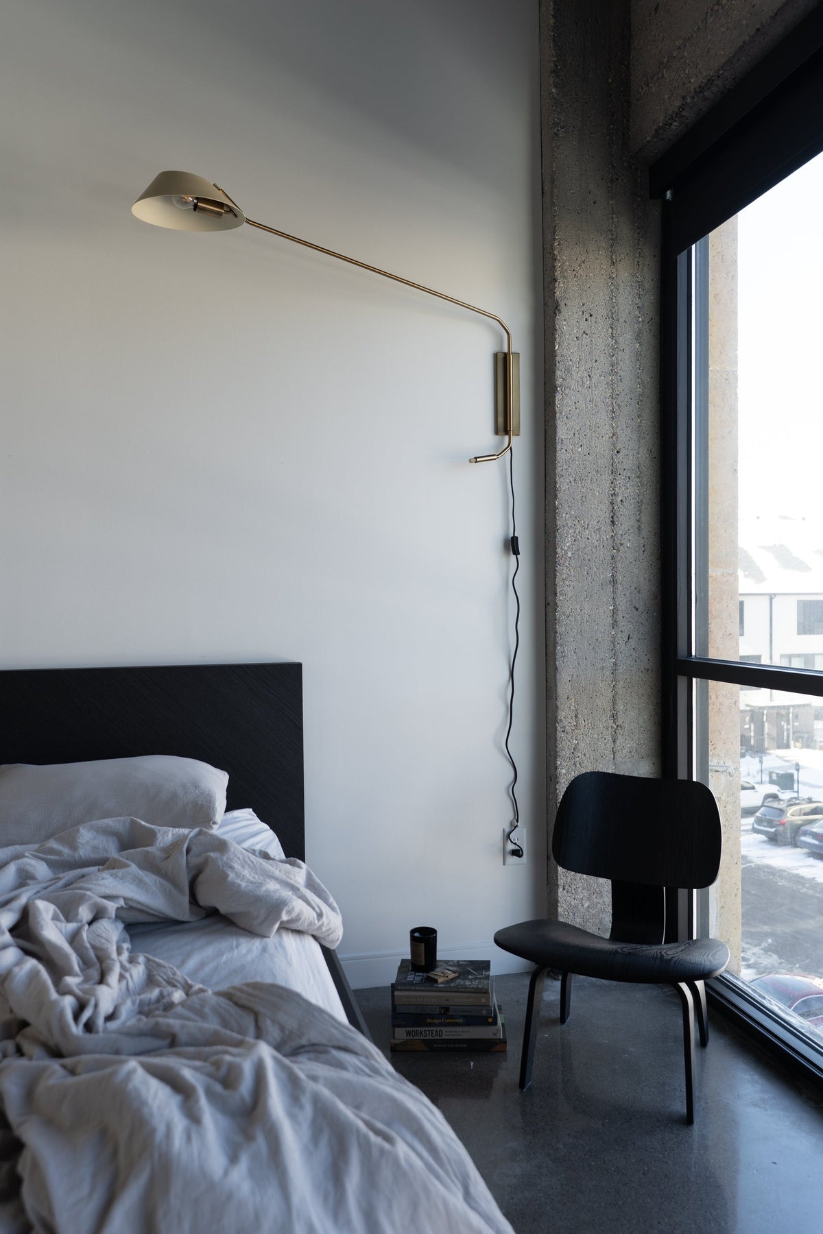 Sacramento brass plug-in sconce with a long arm and sand-colored shade mounted above a bed.