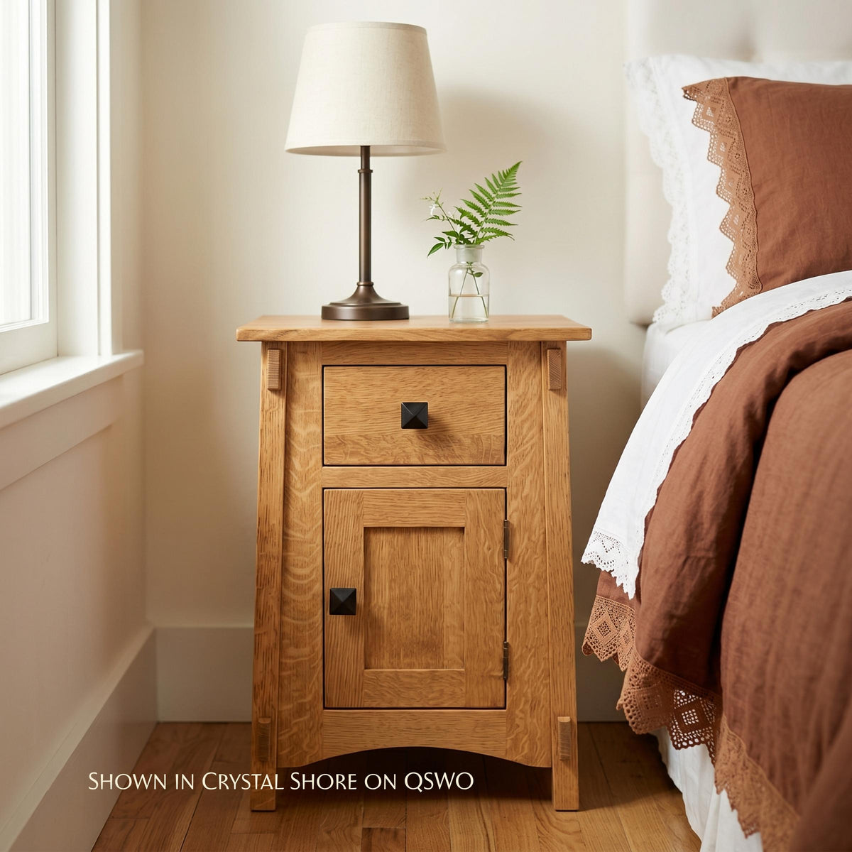 McCoy solid oak nightstand with one drawer, one door, and black hardware next to a bed