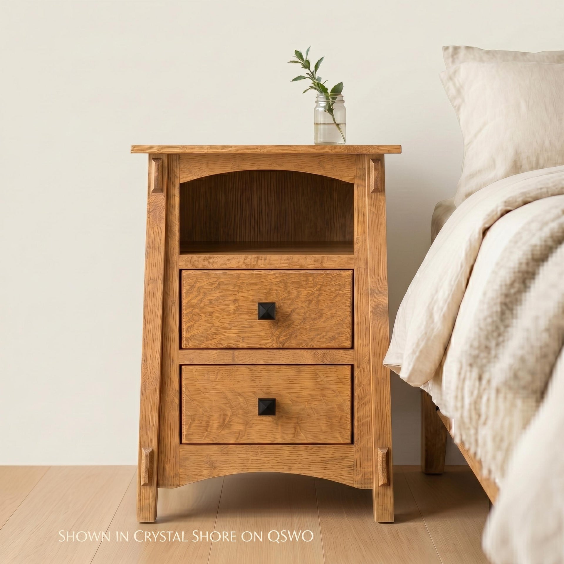 McCoy 2-drawer oak nightstand with open shelf and black hardware next to a bed.