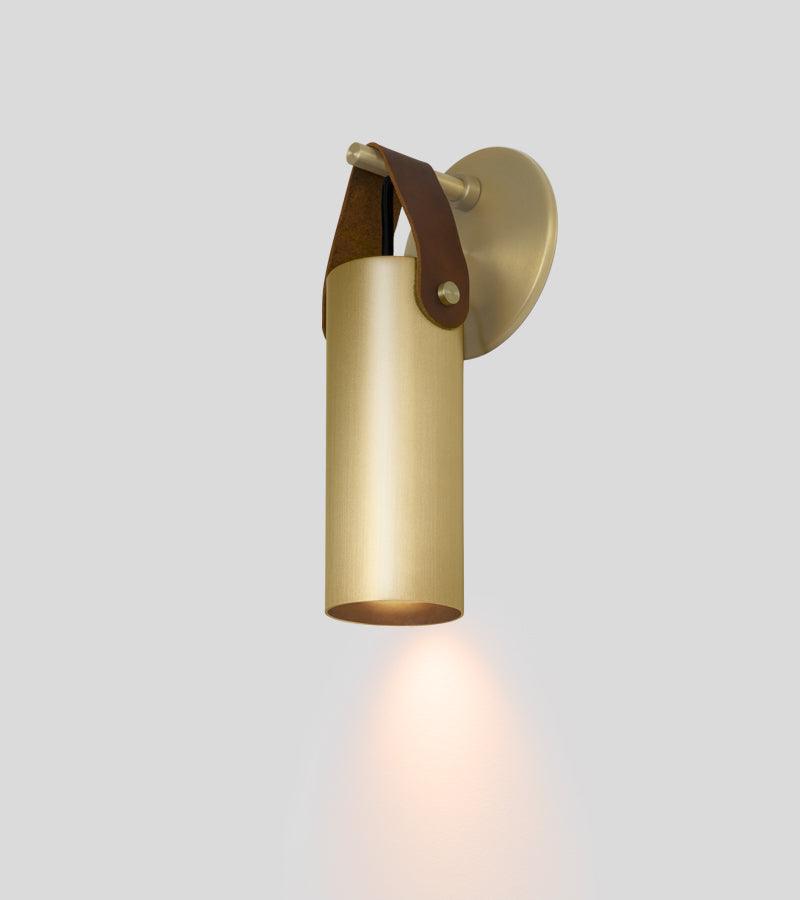 Spero minimalist brass cylinder wall sconce with a brown leather strap hanging mount.