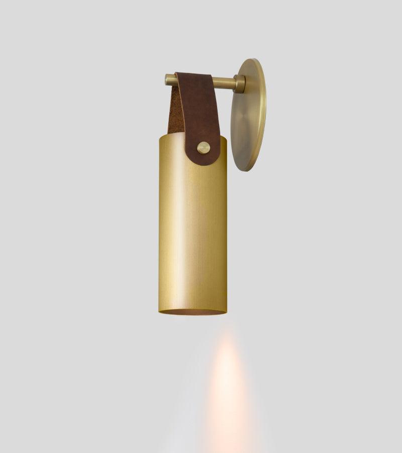 Spero brass cylinder wall sconce with a brown leather strap hanger.