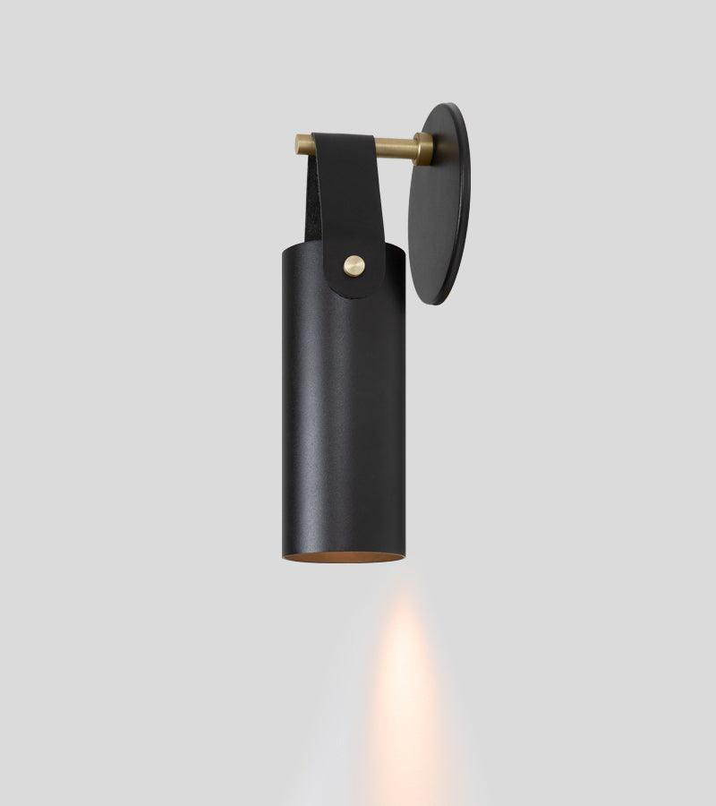 Spero minimalist black leather and brass wall sconce casting a warm downlight.