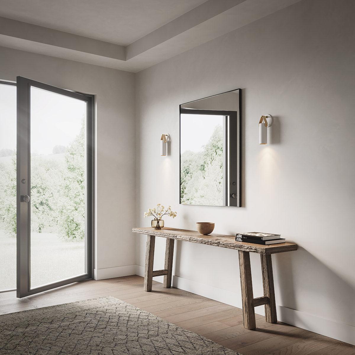 Two minimalist Spero sconces in white and brass flank a mirror in a modern entryway.