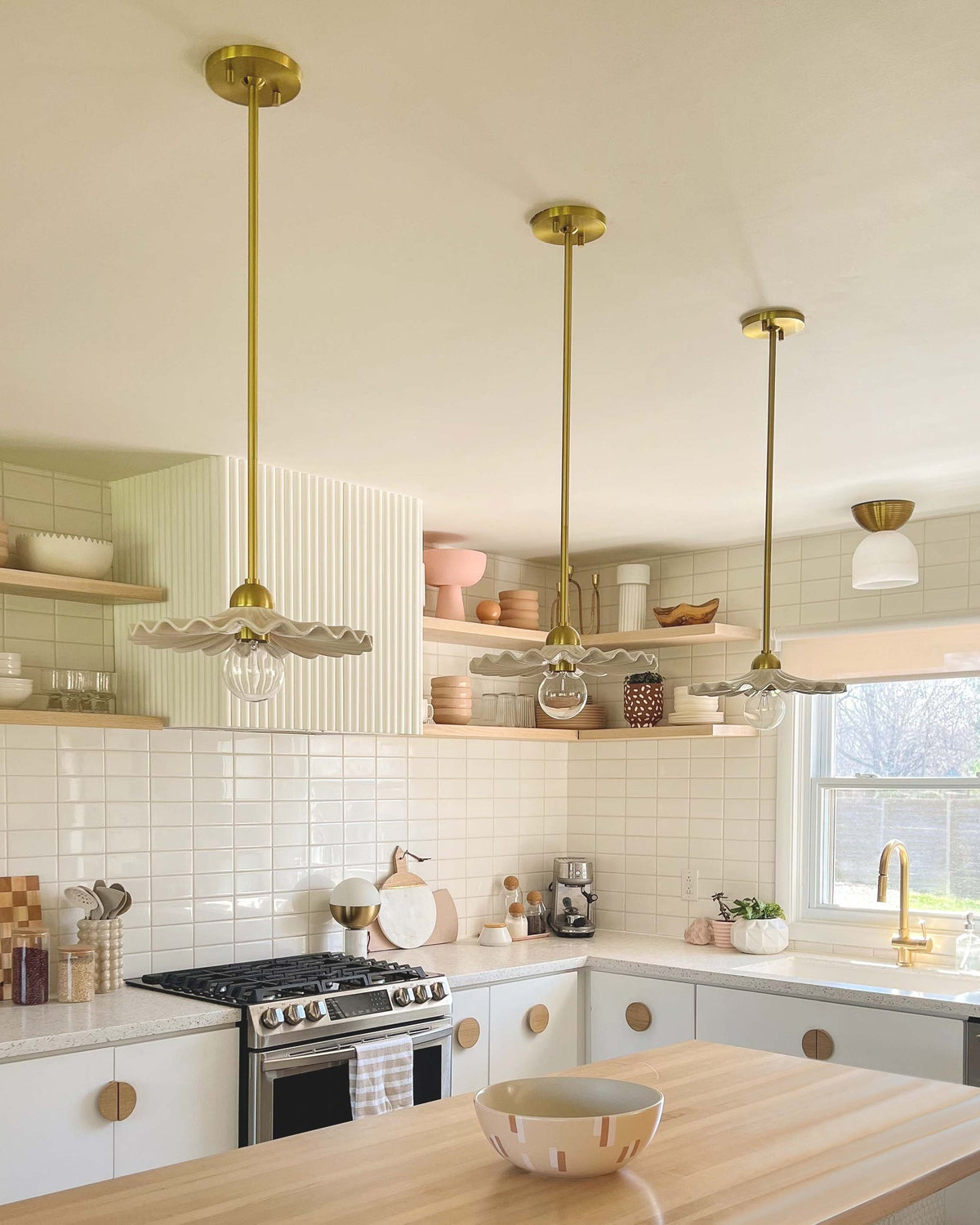 Three Tinsley aged brass pendant lights with wavy white ceramic collars in a kitchen.