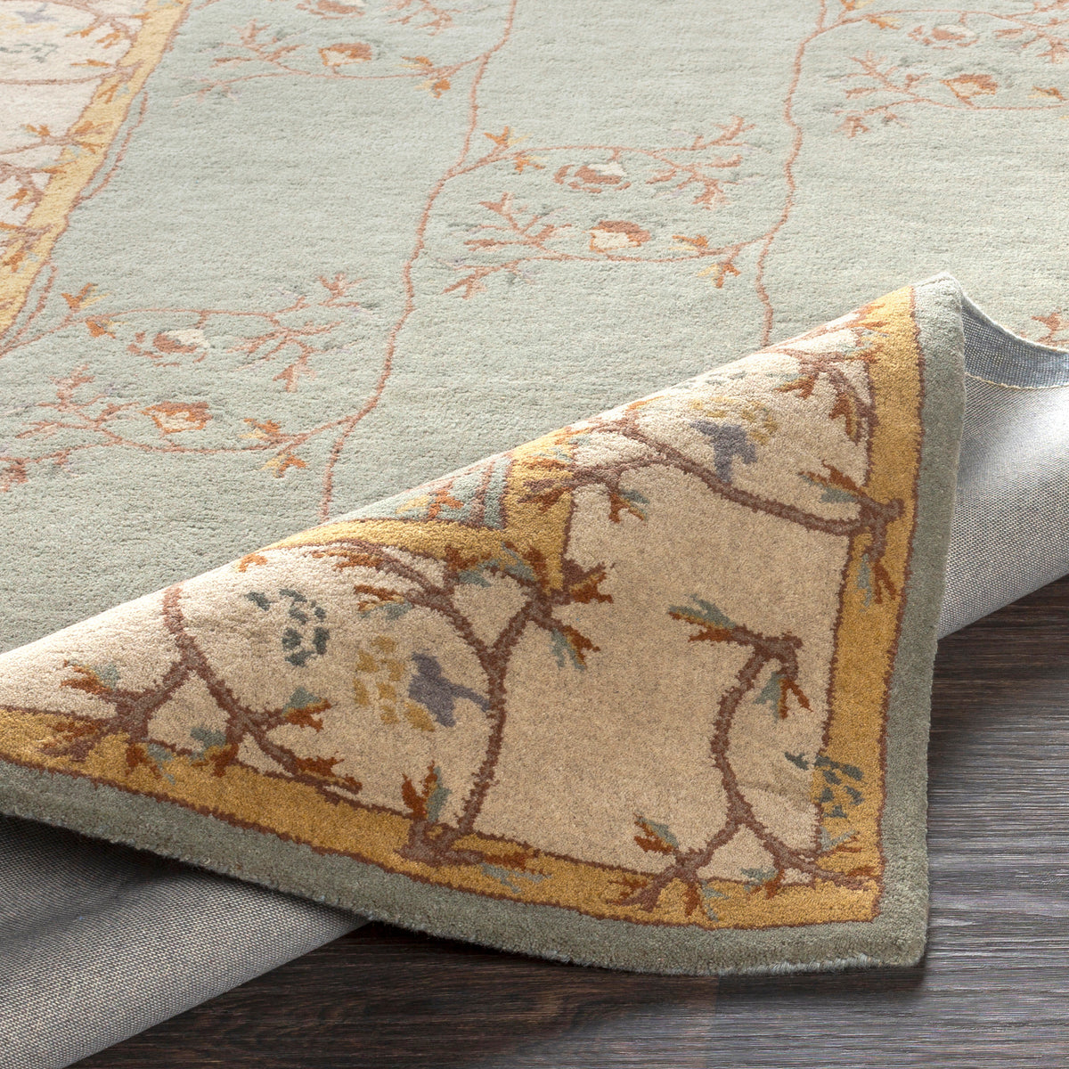 Corinth Azure hand-tufted wool rug with light blue floral pattern and folded corner showing backing
