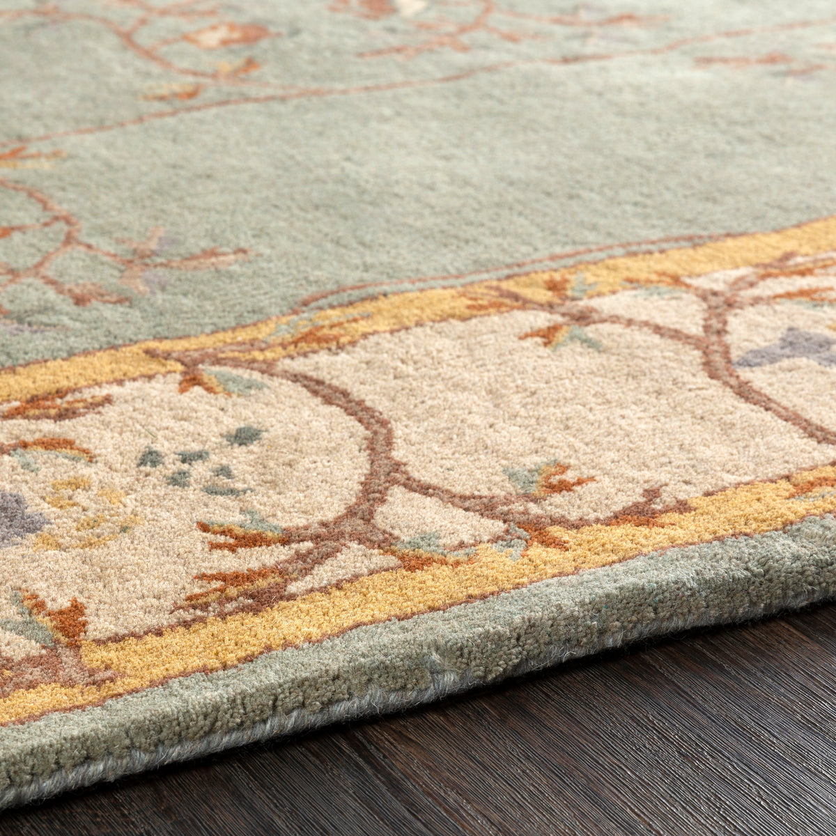 Close-up of the Corinth Azure hand-tufted wool rug with a light blue and beige floral border.