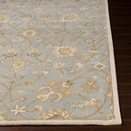 Giardino blue-grey hand-tufted wool rug with an elegant floral pattern on dark wood flooring.