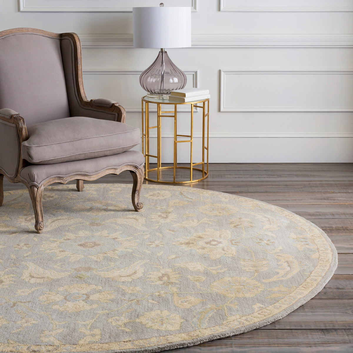 Julian Arctic round wool rug with a light blue and beige floral pattern under an armchair.