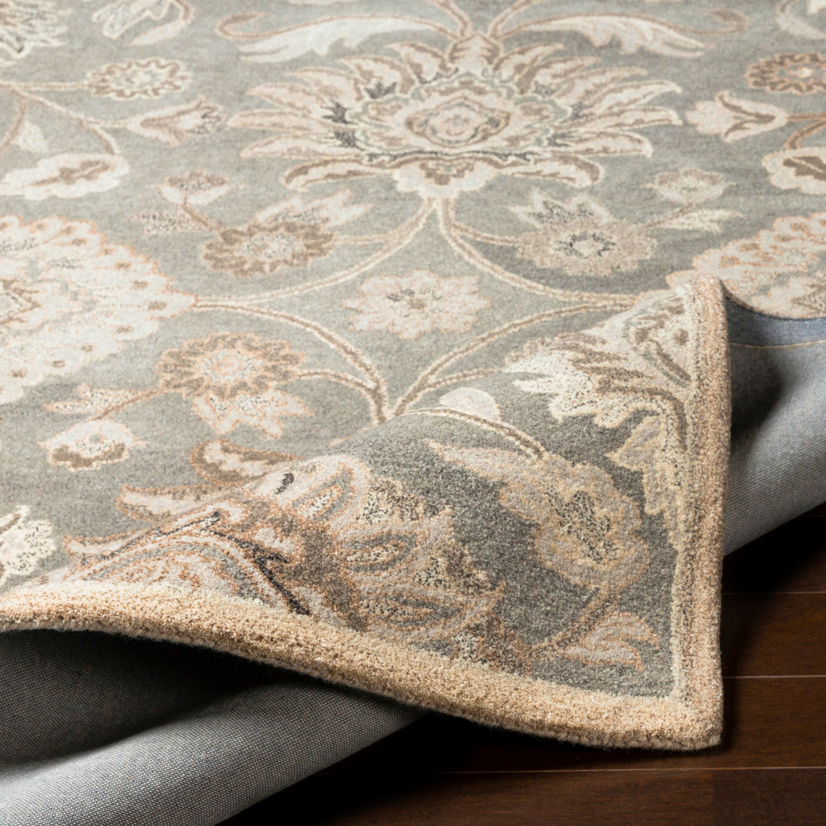 Mediterranean Seal hand-tufted wool rug with grey, taupe, and ivory floral patterns and a folded corner.