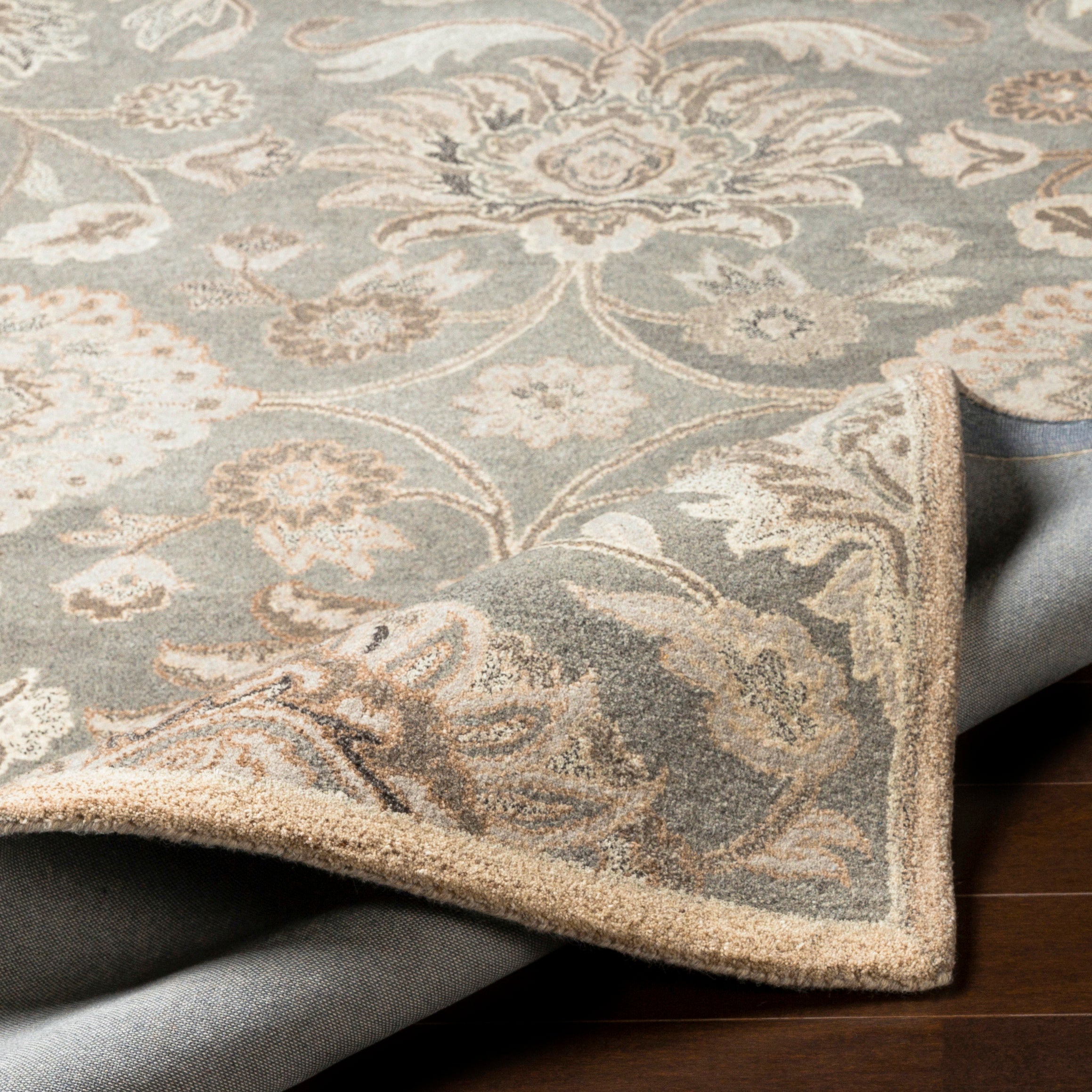 Mediterranean Seal hand-tufted wool rug with grey, taupe, and ivory floral patterns and a folded corner.