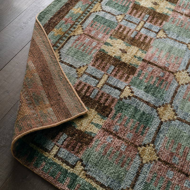 Hazan hand-knotted wool rug with a colorful geometric pattern in green, pink, and brown on wood floors.