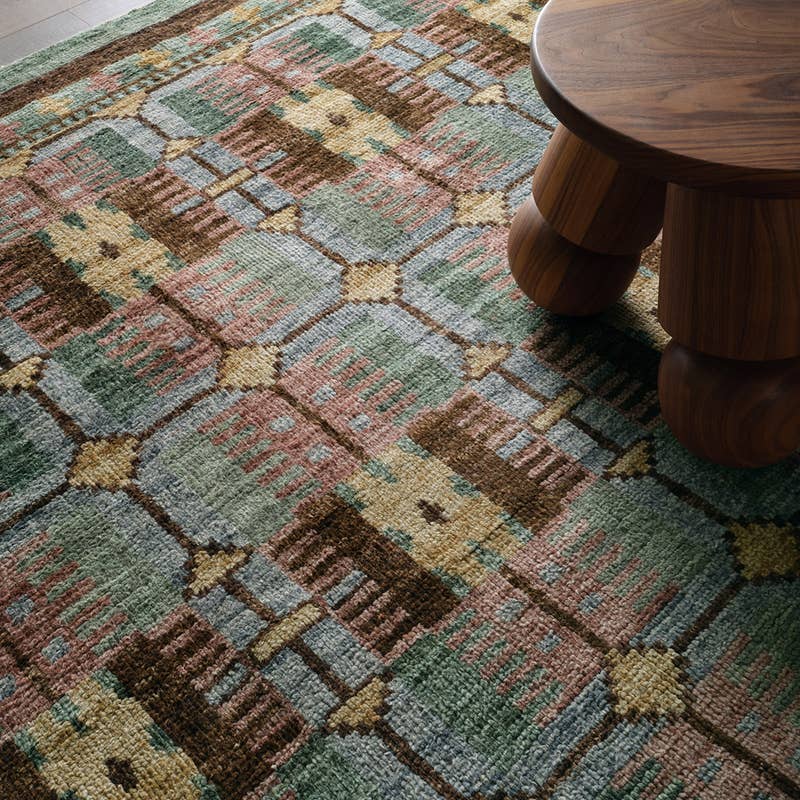 Hazan hand-knotted wool rug with green, pink, and brown geometric patterns next to a wooden stool.