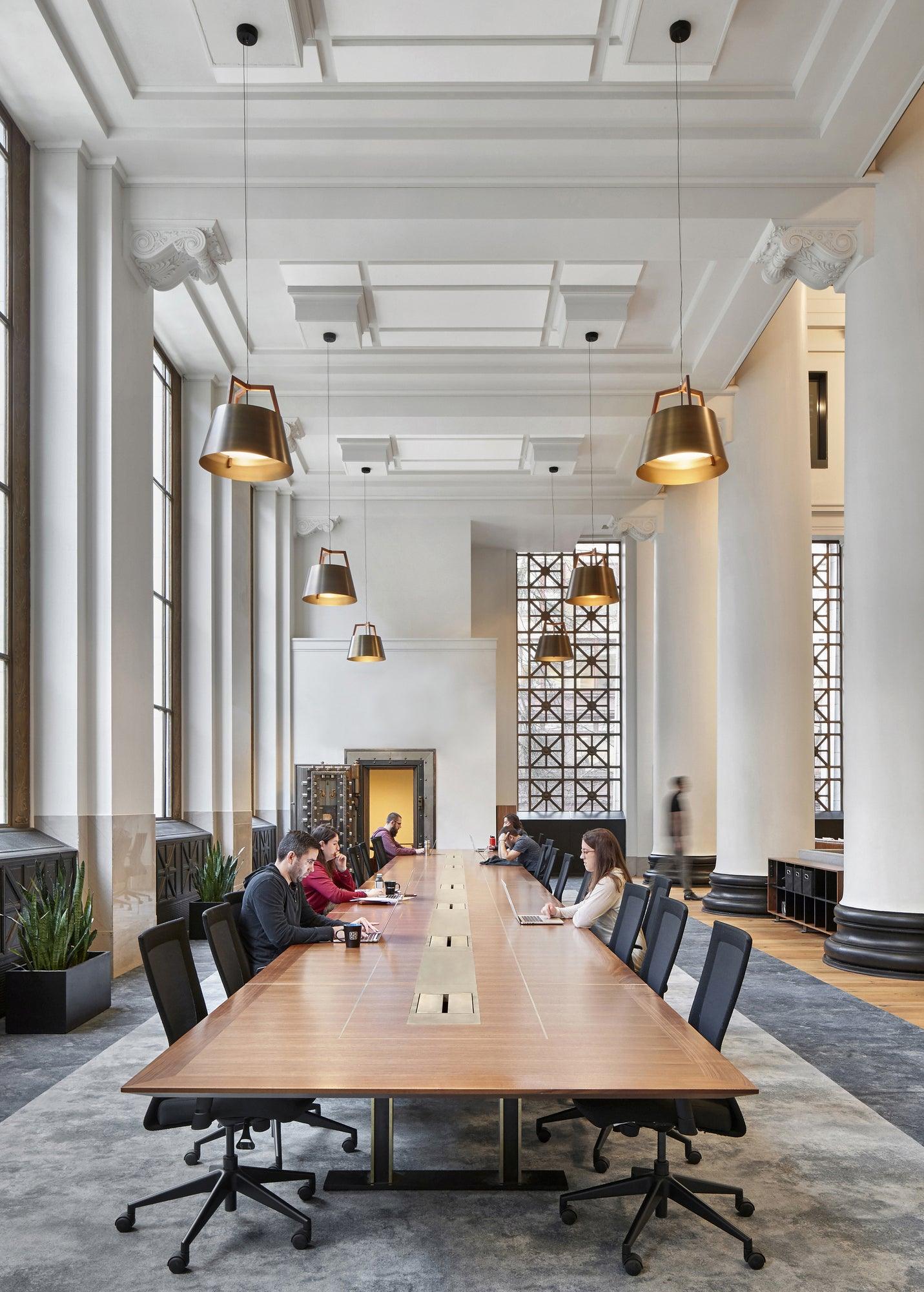 Imber brass pendant lights hanging over a long walnut conference table in a modern office space.
