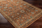 Reign hand-knotted wool rug in rust orange with blue and beige floral patterns on dark wood floor.