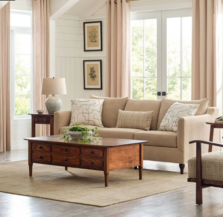Whipstitch Stickley wool rug in tan under a wooden coffee table in a bright living room.