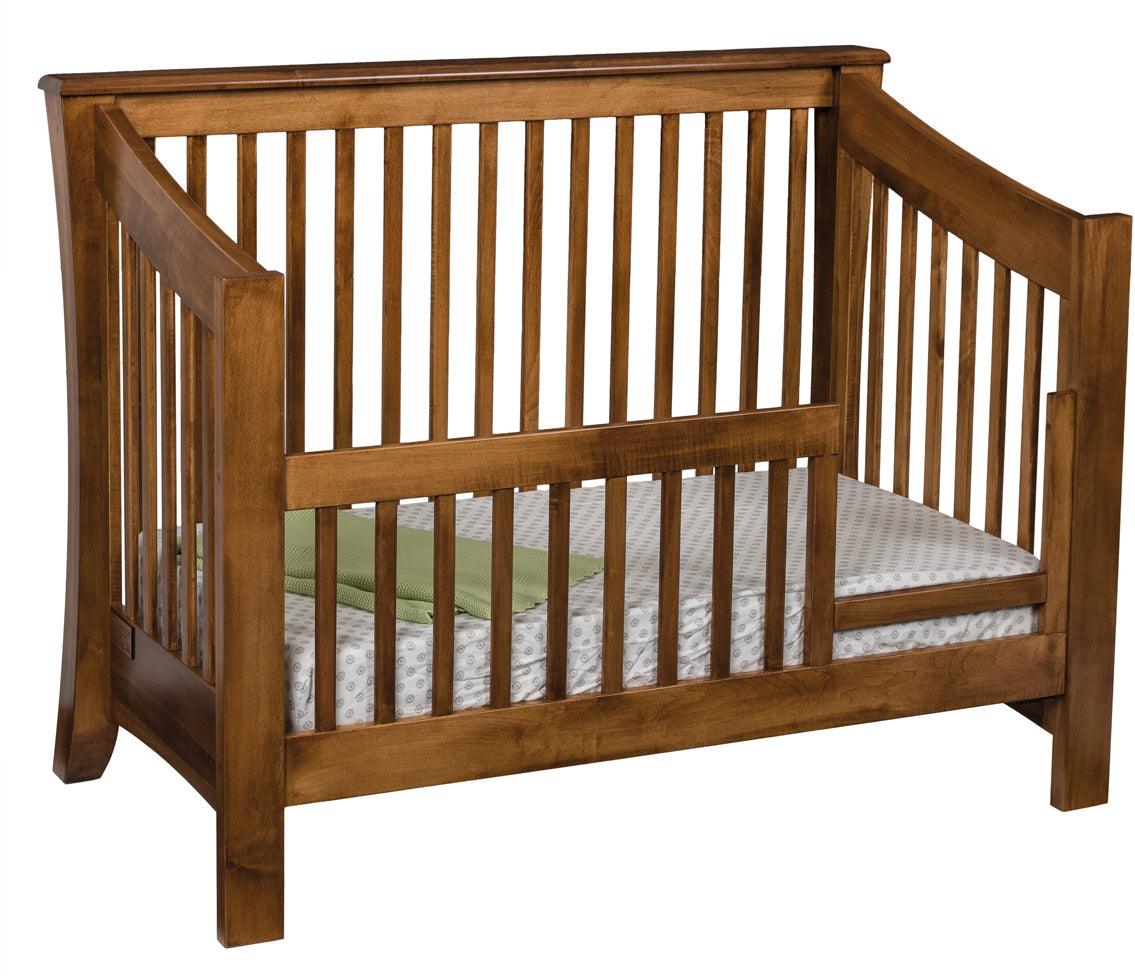 Carlisle convertible toddler bed in a warm brown hardwood finish with a green blanket.